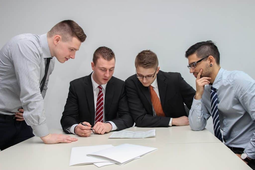 Four men in suits at a table, reviewing papers related to deal management tools.