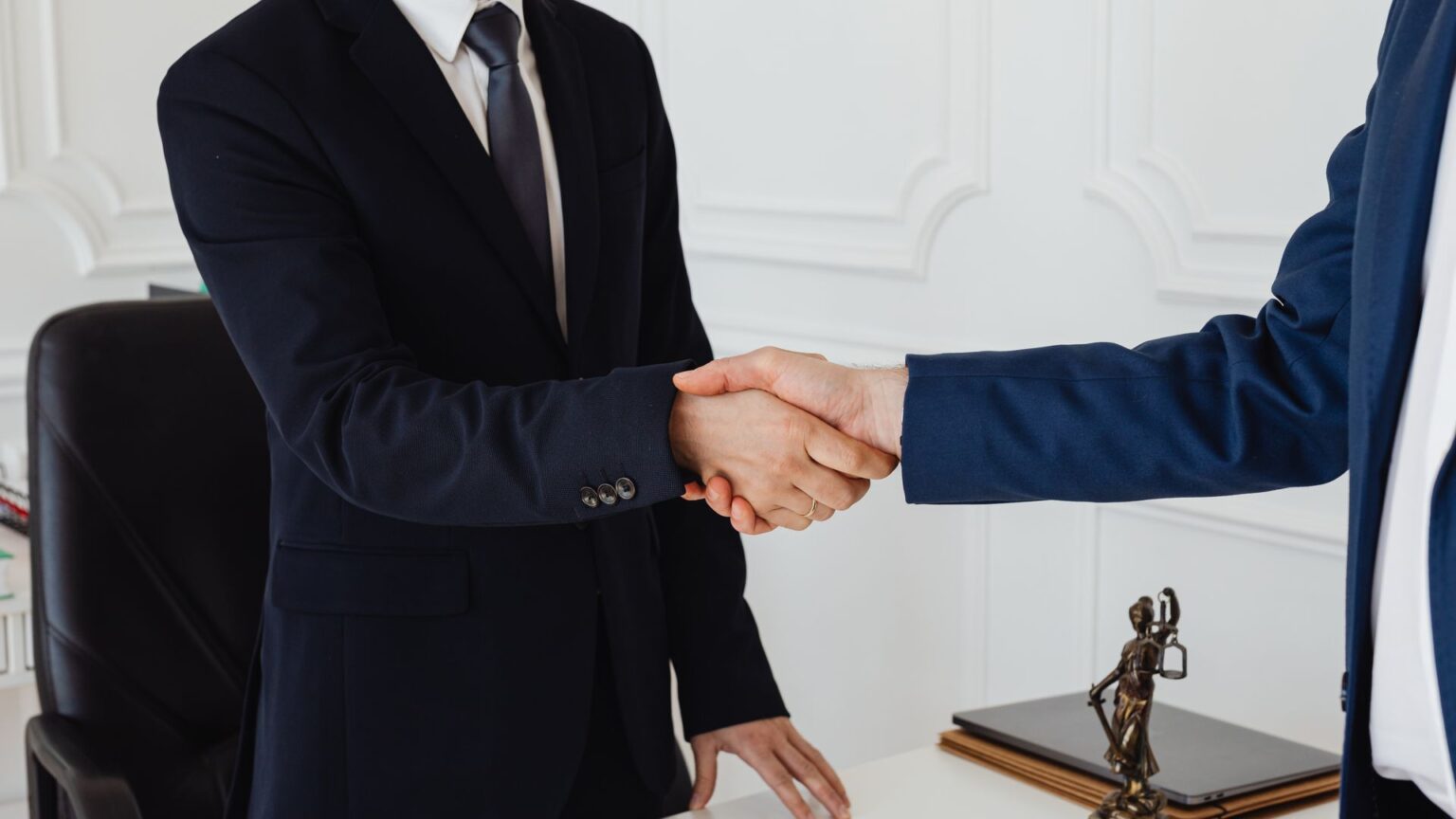 Arbitration Versus Litigation as a Strategy for International Business Disputes Two lawyers shake hands beside a scales of justice statuette, illustrating arbitration Versus Litigation as a Strategy for International Business Disputes